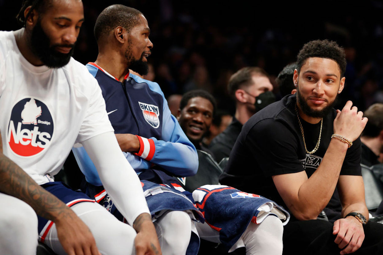Ben Simmons (R) sits alongside Kevin Durant on the Brooklyn Nets bench.