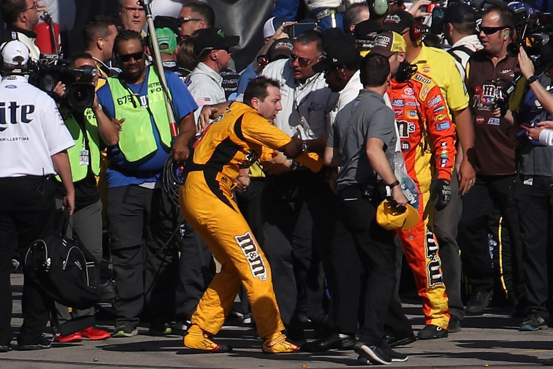Kyle Busch being escorted away by NASCAR officials after fighting with Joey Logano's pit crew