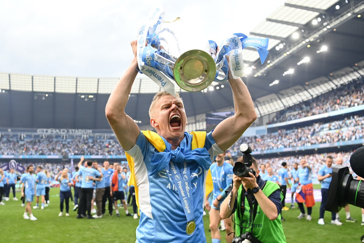 Oleksandr Zinchenko of Manchester City celebrates with the Premier League trophy and a Ukrainian flag.