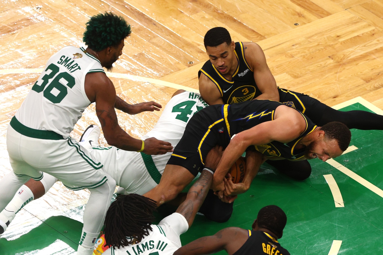 Stephen Curry and Jordan Poole of the Golden State Warriors compete for a loose ball against Al Horford of the Boston Celtics.