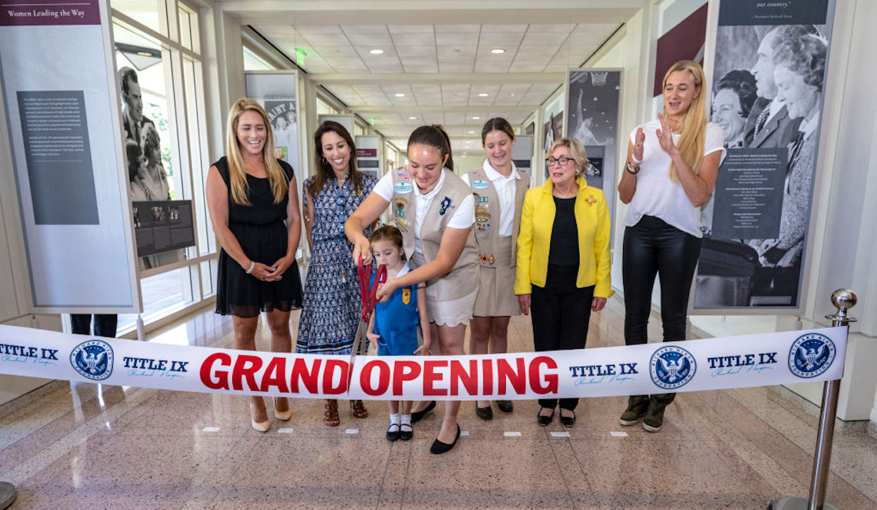 Multiple women participate in the ribbon cutting of a Title IX-related exhibit at the Richard Nixon Presidential Library and Museum.