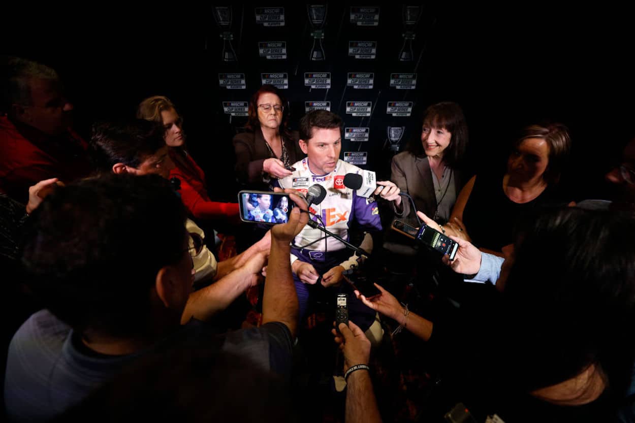 Denny Hamlin sits surrounded by reporters.