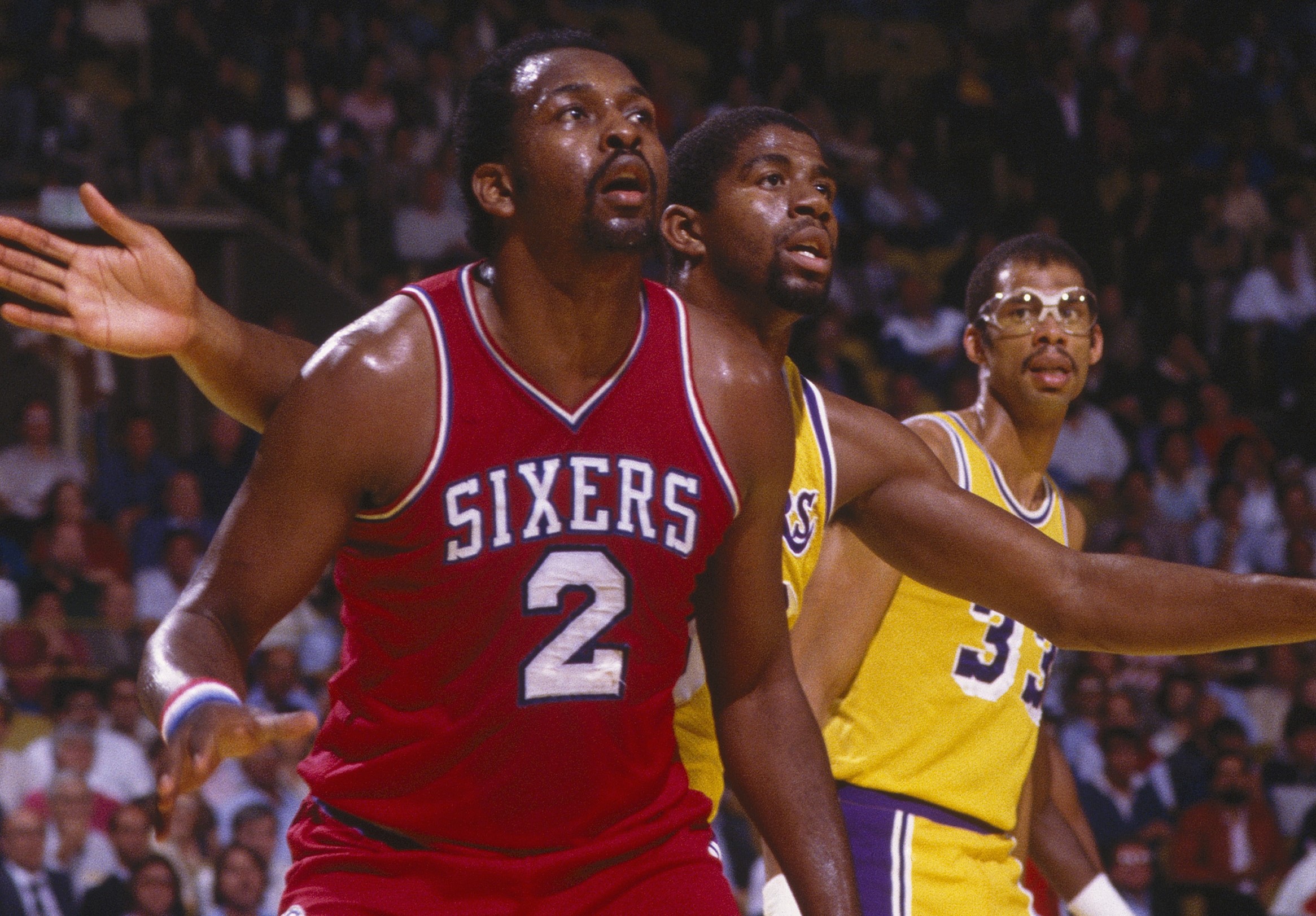 Moses Malone of the Philadelphia 76ers looks for a pass as Magic Johnson of the Los Angeles Lakers guards him.