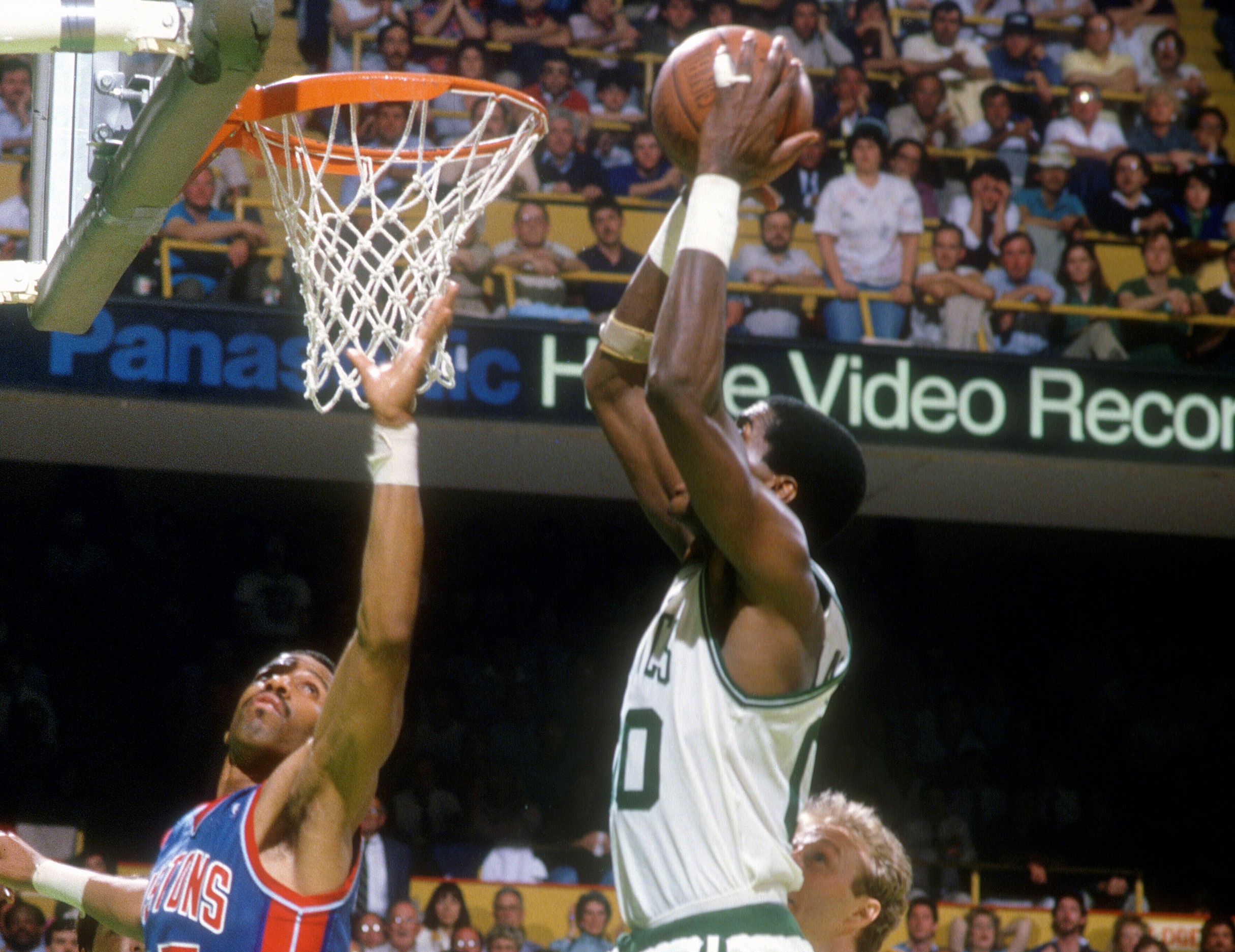 Robert Parish of the Boston Celtics slam dunks over Adrian Dantley of the Detroit Pistons.