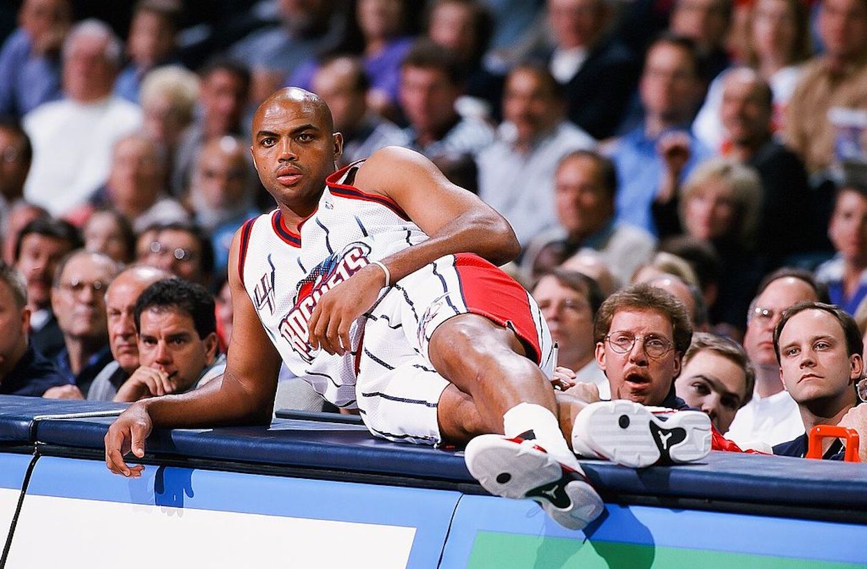 Charles Barkley reclines on the scorer's table during an NBA game.