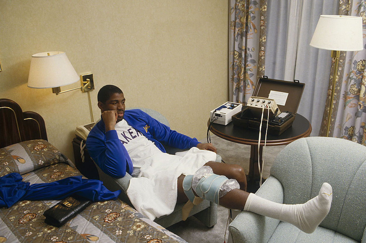 Magic Johnson sits in a hotel room resting his knee.