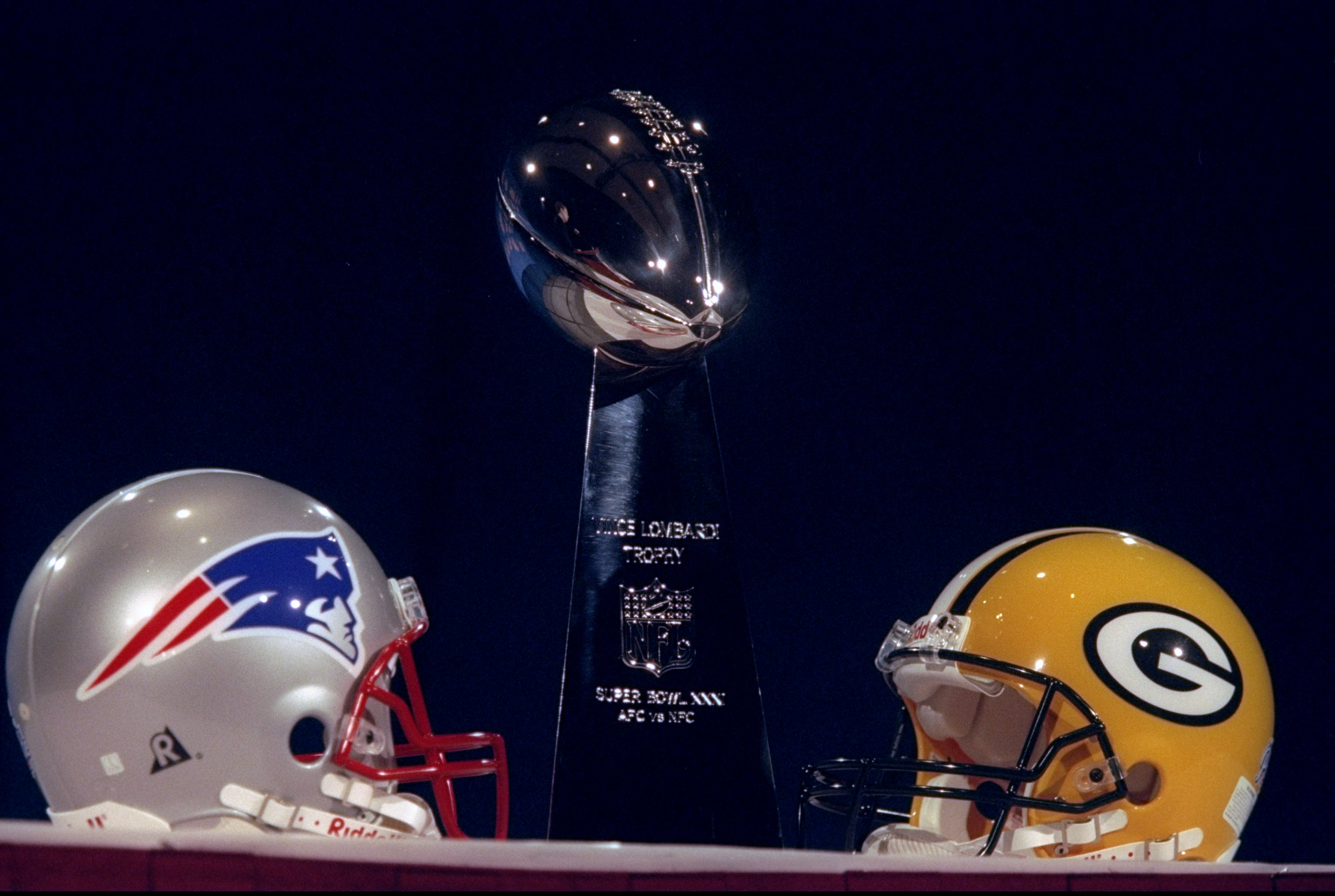 The Vince Lombardi trophy is bracketed by the helmets of the two teams that played in Super Bowl 31, the Green Bay Packers and the New England Patriots.