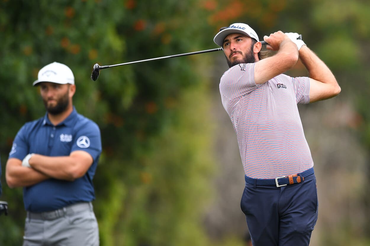 Max Homa hits a tee shot as Jon Rahm looks on.