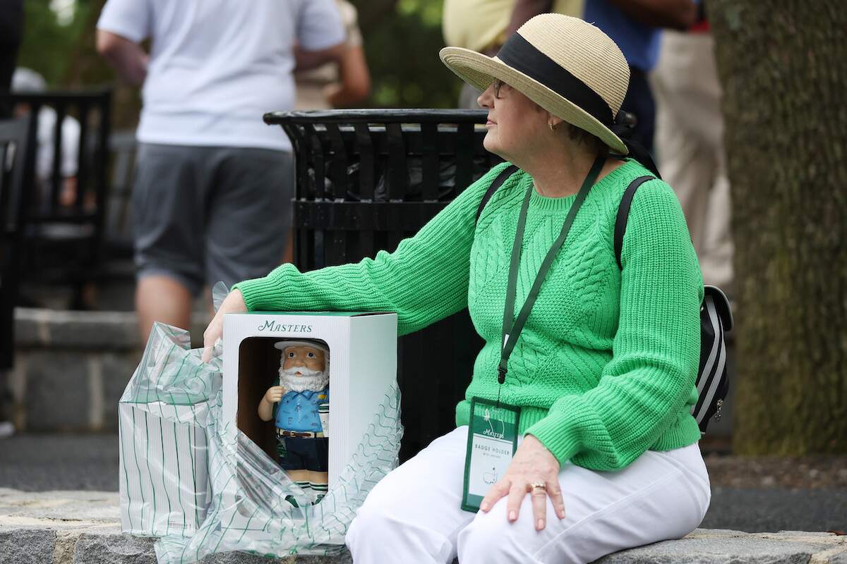 Woman in a green sweater carries a 2023 Masters gnome outside the golf shop