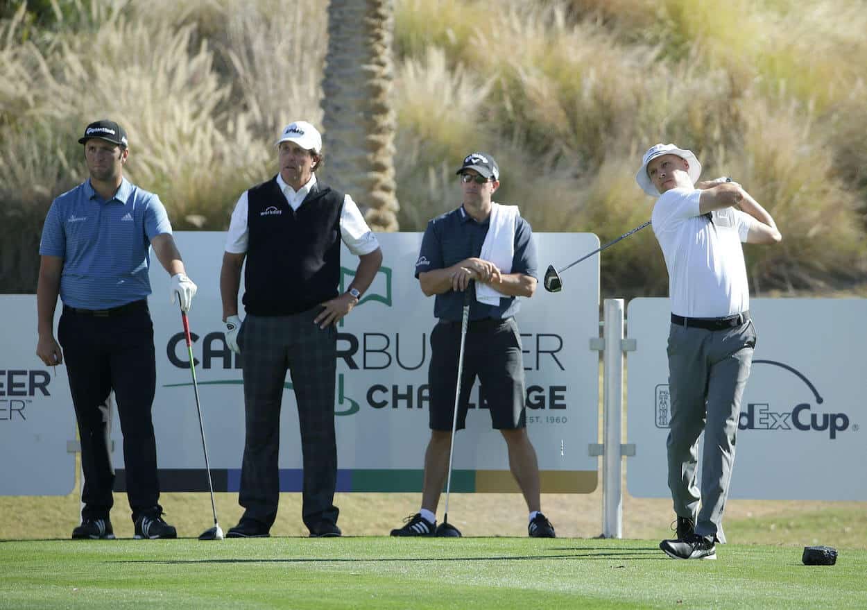 Jon Rahm, Phil Mickelson, and Tim Mickelson watch Ben Crane hit a tee shot.