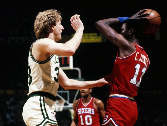 Caldwell Jones of the Philadelphia 76ers looks to pass the ball over the top of Larry Bird of the Boston Celtics.
