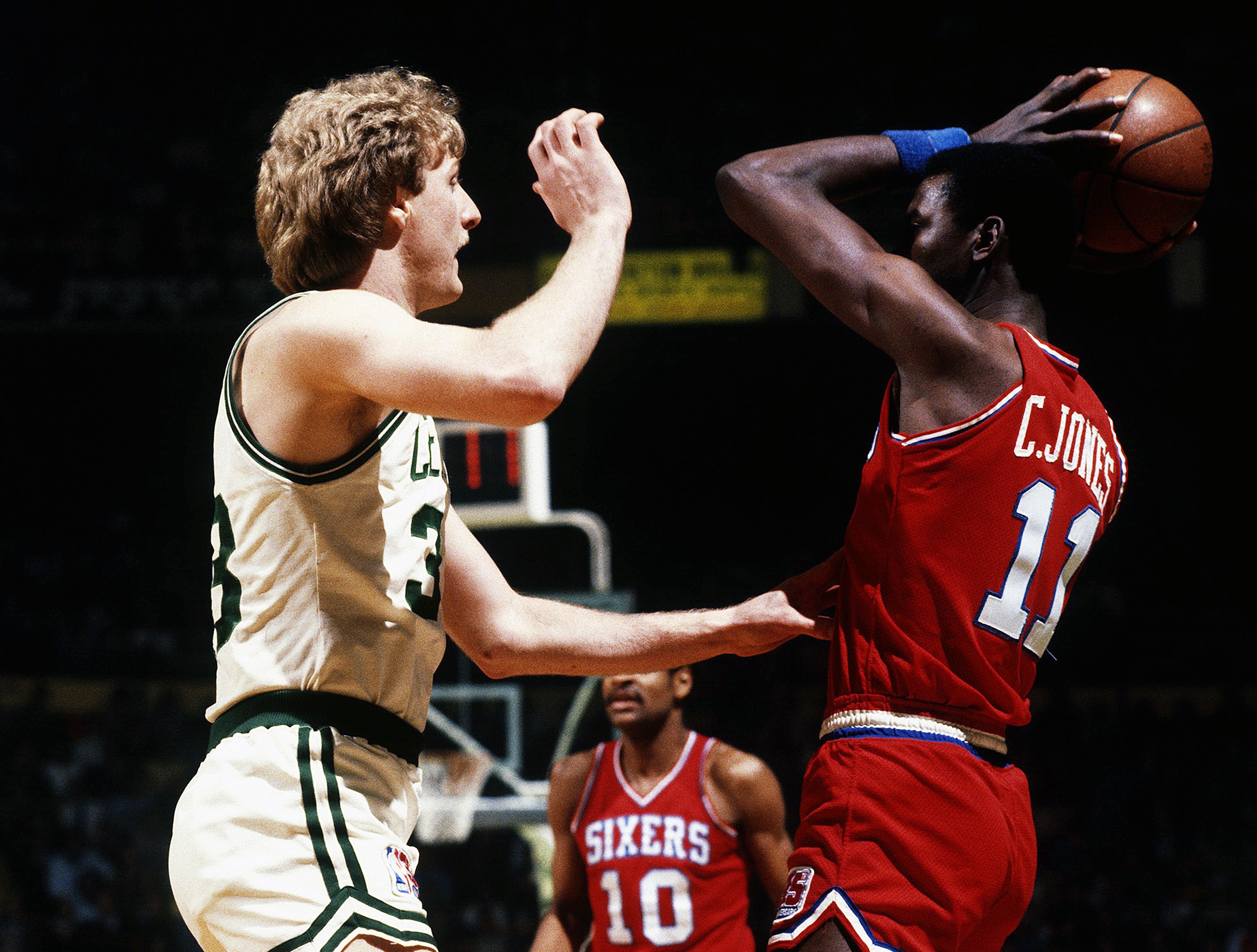 Caldwell Jones of the Philadelphia 76ers looks to pass the ball over the top of Larry Bird of the Boston Celtics.