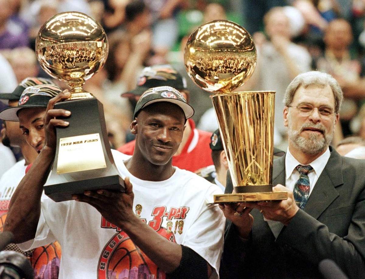 Bulls player Michael Jordan and coach Phil Jackson hold up their championship trophies
