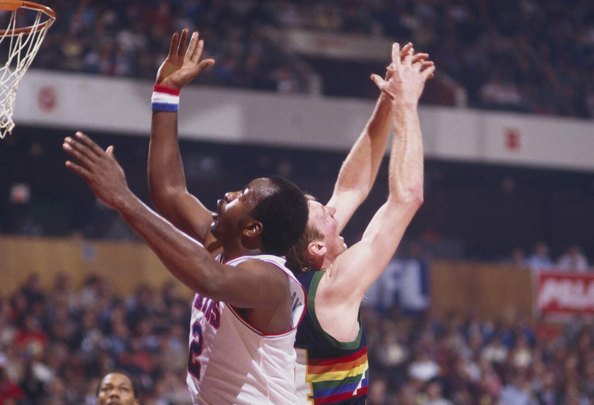 Moses Malone (L) of the Philadelphia 76ers jumps up for a rebound during a game against the Denver Nuggets in 1985