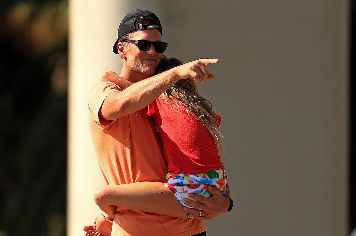 Tom Brady points at photographers as he holds his daughter Vivian