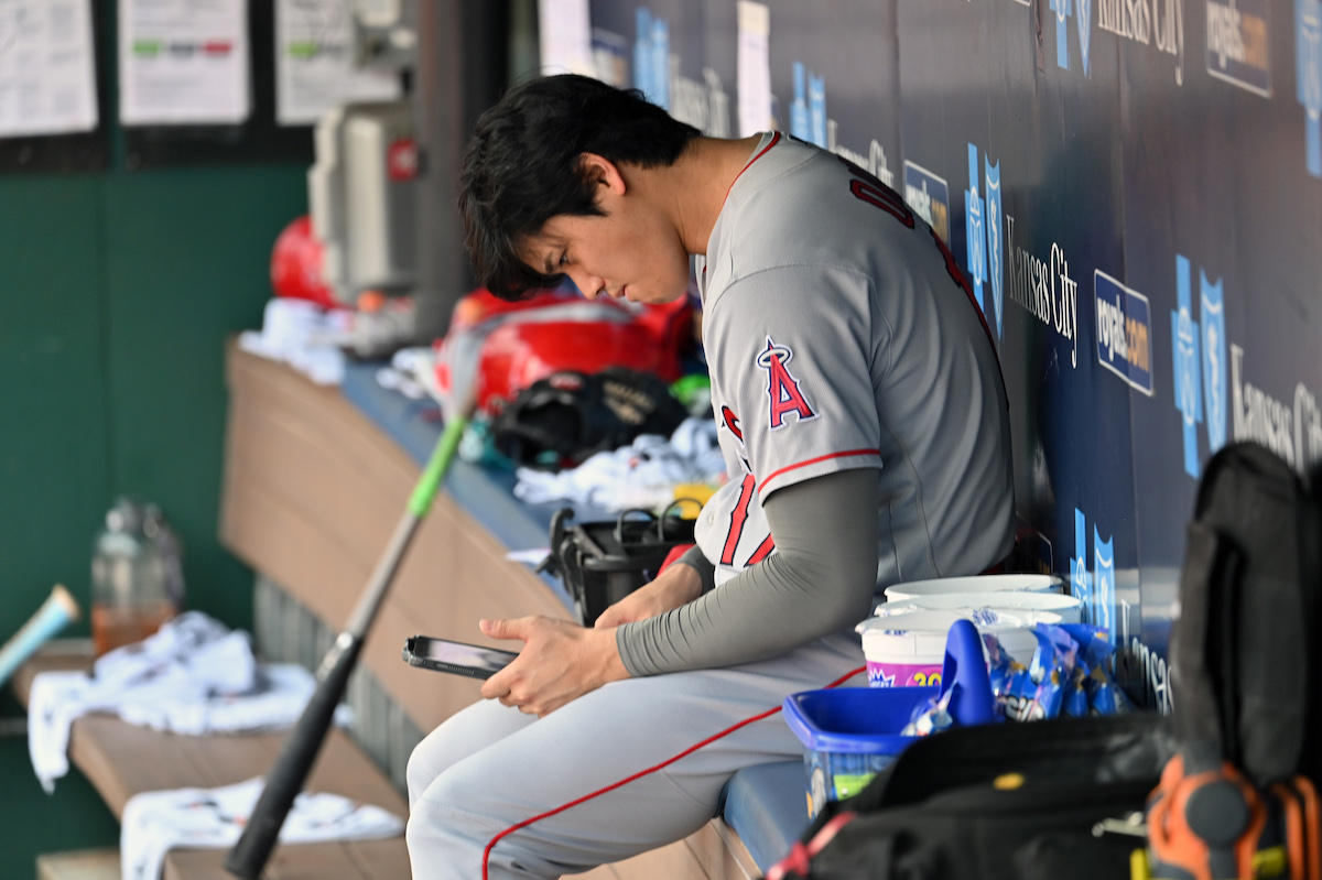 Shohei Ohtani of the Los Angeles Angels checks his phone in the dugout.