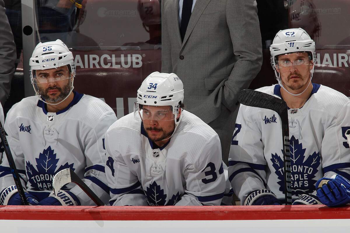 Auston Matthews of the Toronto Maple Leafs sits on the bench between teammates Mark Giordano and Noel Acciari