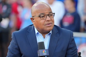 NBC Sports broadcaster Mike Tirico holds a mic.