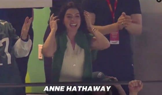 Anne Hathaway puts her hands up while watching the Super Bowl.