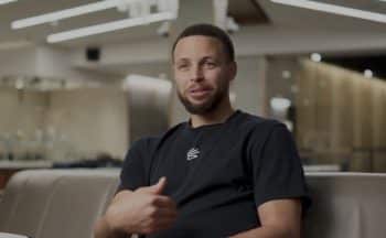 Steph Curry sits on a couch and points at himself.