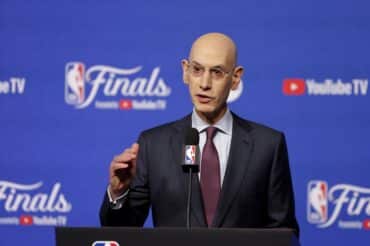 Adam Silver puts his hand up at the podium.