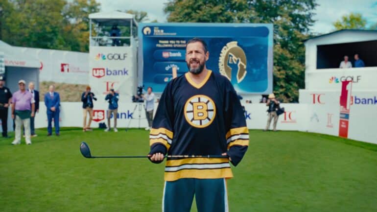 Adam Sandler holds a hockey club.