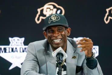 Deion Sanders sits at the mic.