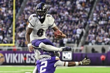 Baltimore Ravens quarterback Lamar Jackson leaps over a player.