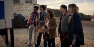 A group of kids and adults stand next to each other in Stranger Things.