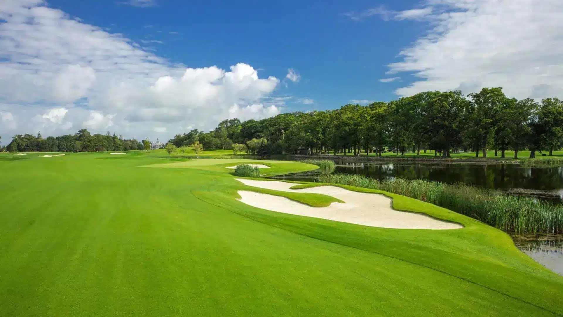 Lush green golf course with sand traps and a serene water feature under a blue sky.