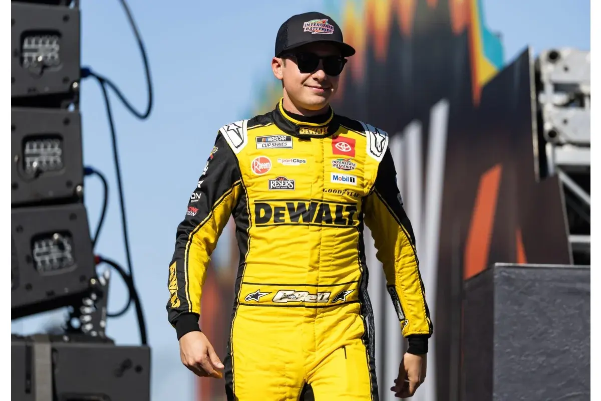 Christopher Bell in a yellow racing suit, walking on stage at a NASCAR event.