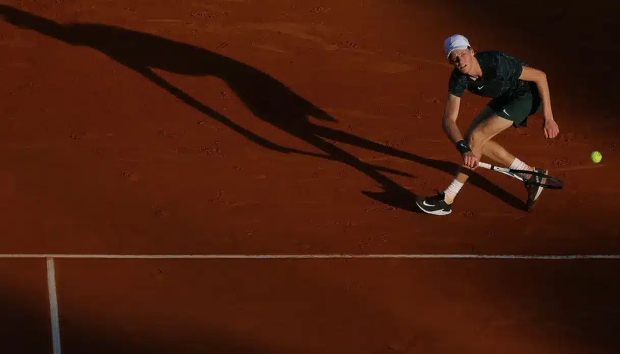 A tennis player in a green outfit hitting a ball on a clay court during a match.