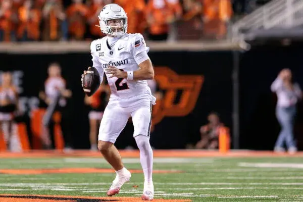 Cincinnati quarterback in white uniform throws a football on the field during a game.