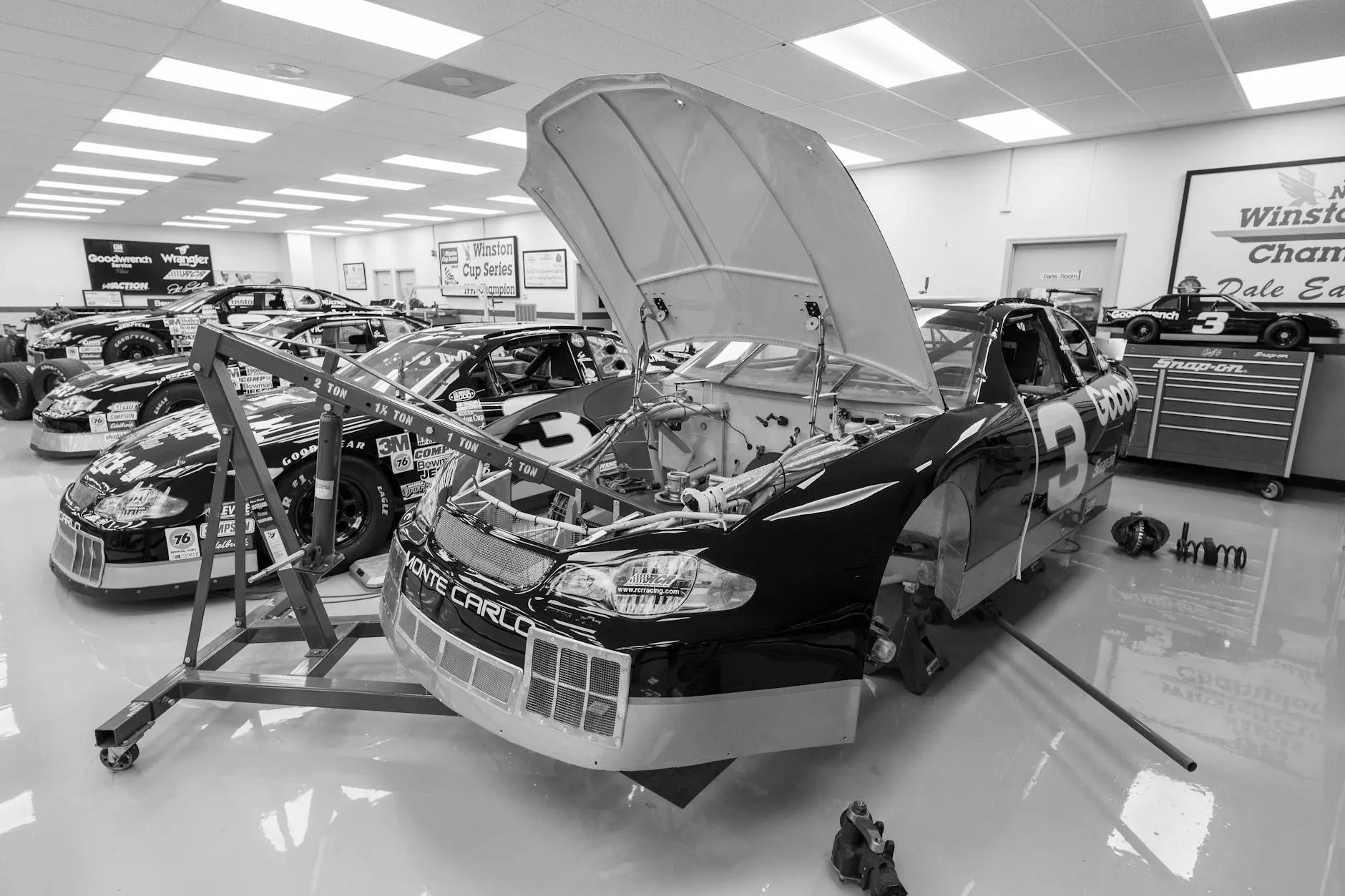 A black-and-white image of race cars being worked on in a garage, featuring the number 3 car.