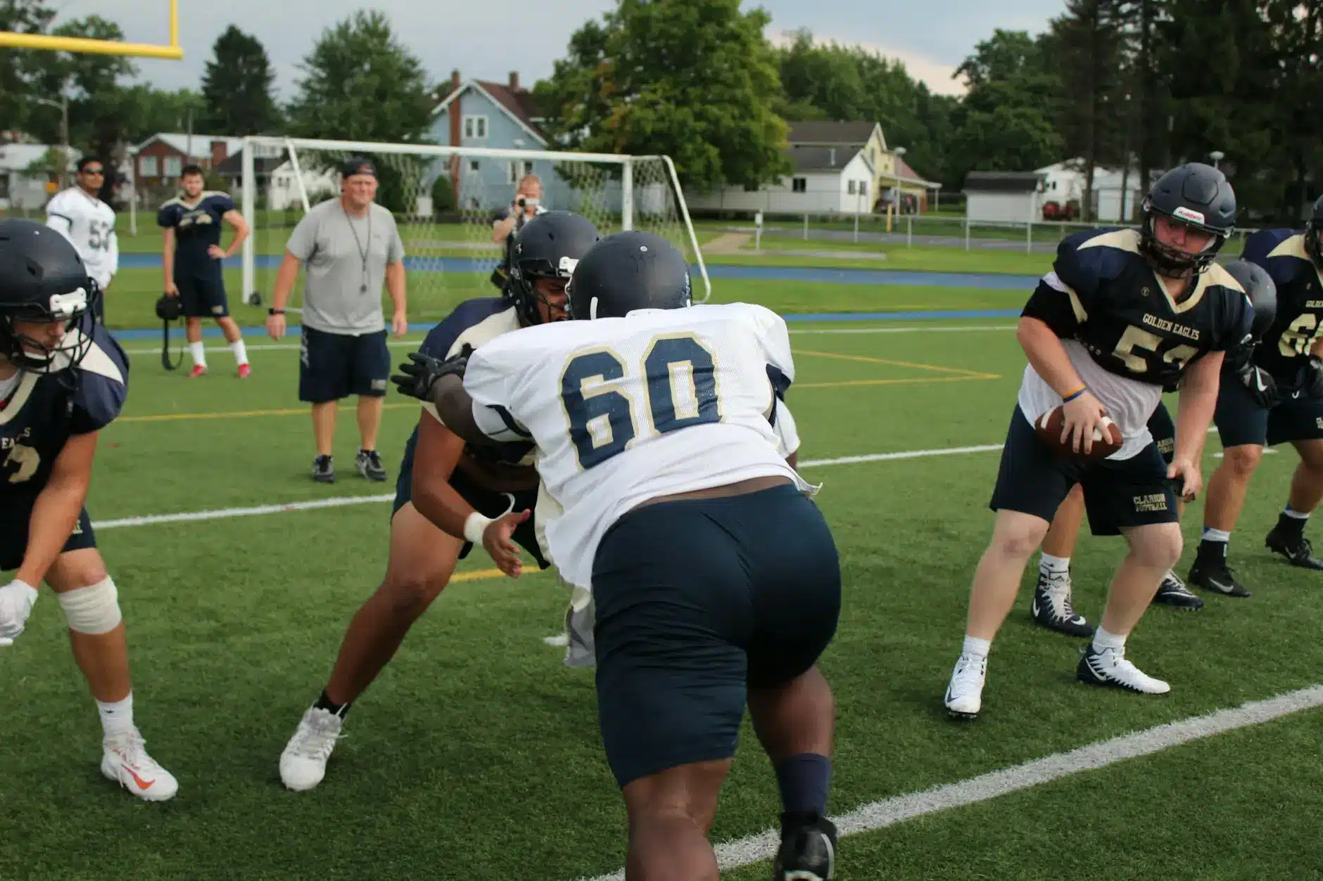 High school football players practice blocking and rushing techniques on a field.