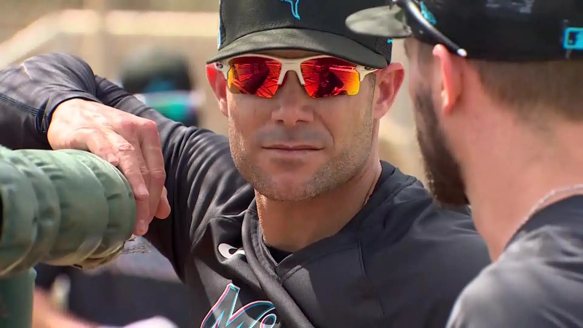 Miami Marlins manager Skip Schumaker talking with a player, wearing sunglasses and team gear.