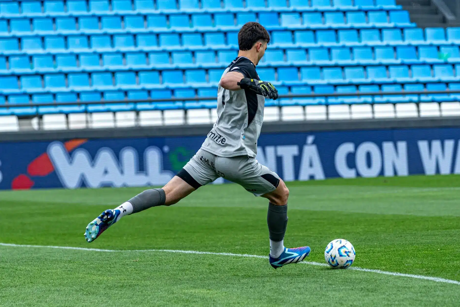 A footballer in gray kit warming up on the pitch, preparing to kick a ball.