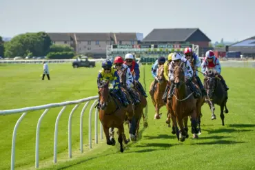 Jockeys racing on horses at a UK horse racing event with green grass track.