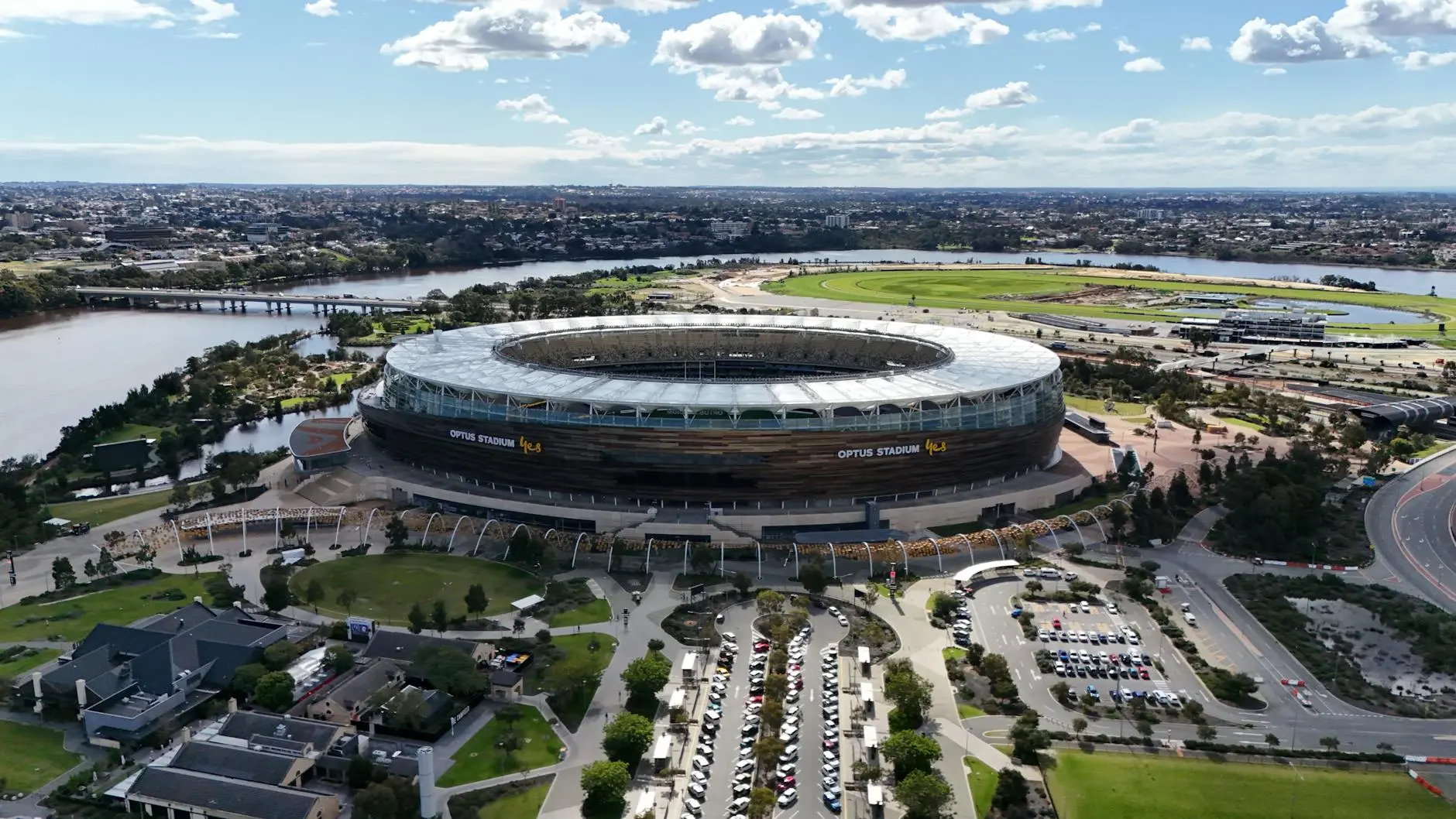 Optus Stadium in Melbourne, Australia, surrounded by greenery and a river.