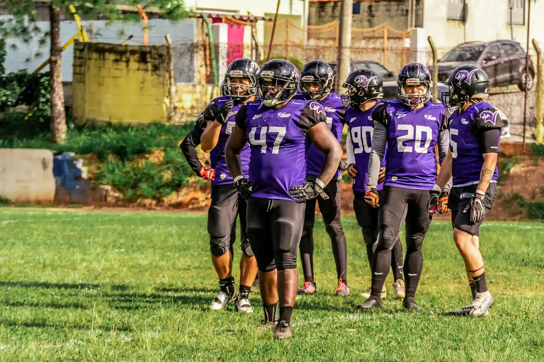 Group of six football players in purple jerseys preparing on a grass field.