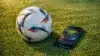 Soccer ball and smartphone with betting app on stadium turf under stadium lights