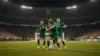 Soccer players in green jerseys competing for the ball under stadium lights during intense match action