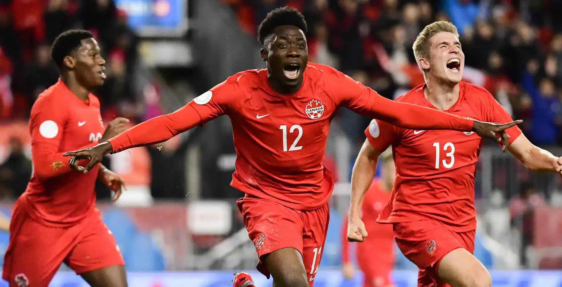 Alphonso Davies celebrating a goal in a Canada soccer match with teammates.