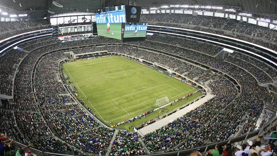 View of a packed AT&T Stadium during a soccer match with players on the field.