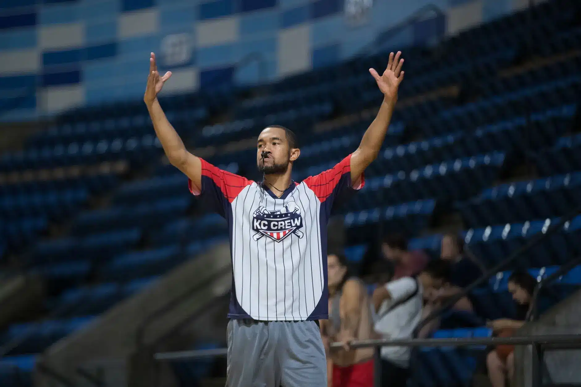 A basketball referee in a KC Crew shirt signaling during a game.