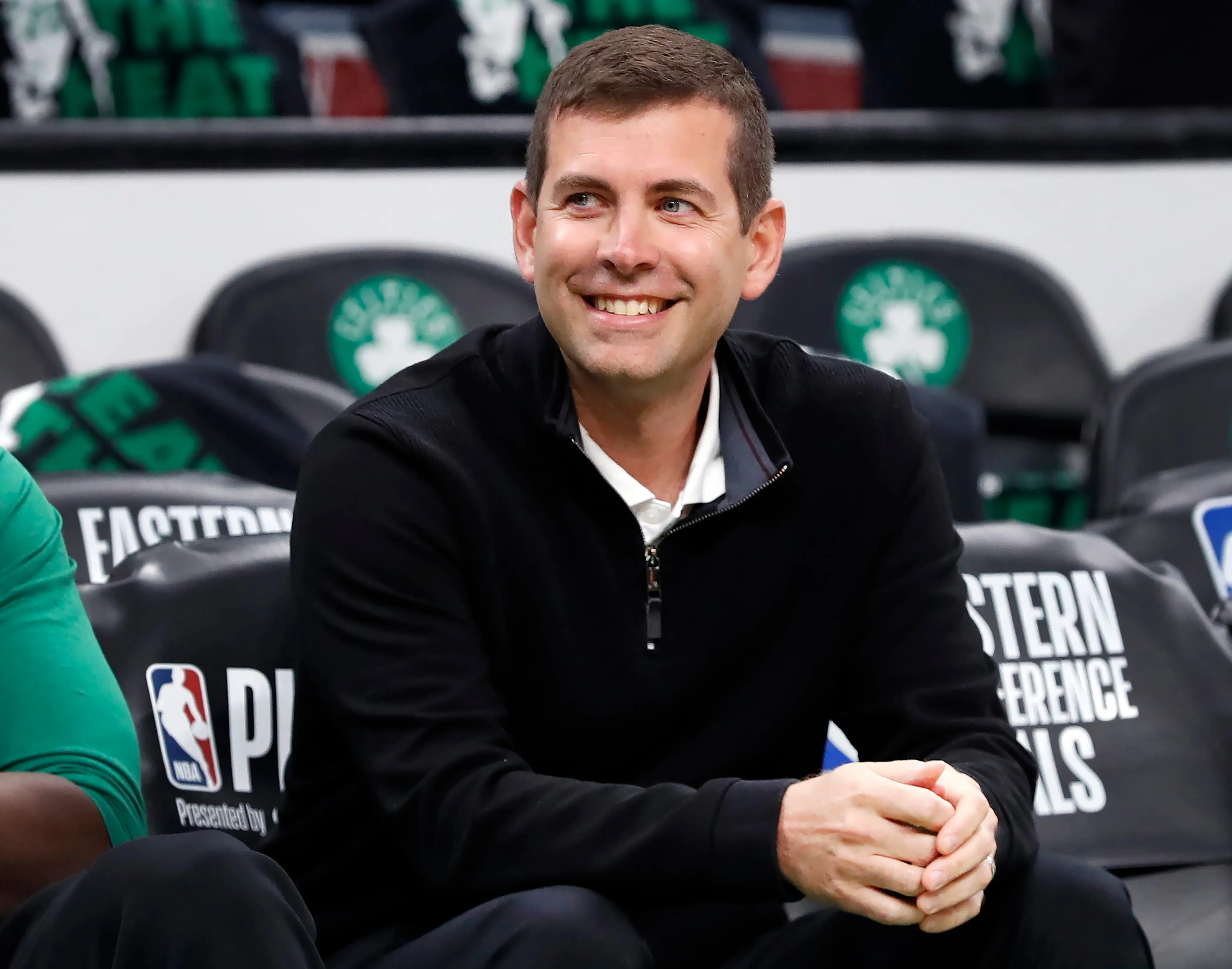 Brad Stevens smiling while seated on the Celtics bench during a game.