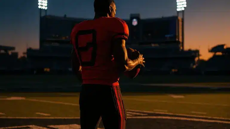 College quarterback at crossroads between college and NFL football field under dramatic stadium lights