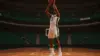 Basketball center shooting three-pointer in modern NBA arena with Celtics green accents and dramatic lighting