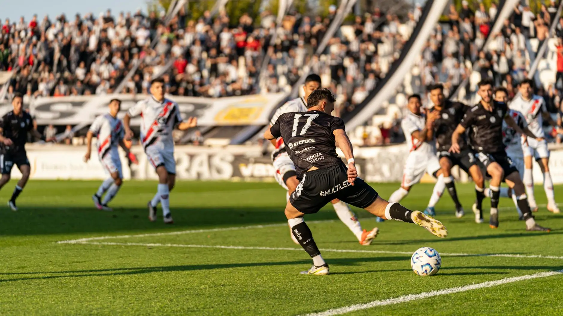 Soccer match action with players in black and white jerseys and a cheering crowd.