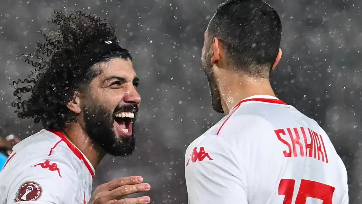 Two Tunisia national team players celebrating in the rain, one wearing 'Skhiri' jersey.